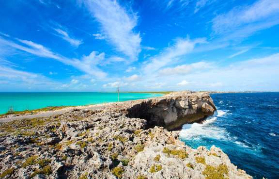 The Eleuthera land bridge, also known as the Glass Window Bridge, is a natural limestone arch that spans across Queen's Highway, connecting the northern and southern parts of Eleuthera Island in the Bahamas. The bridge provides a striking visual contrast between the dark blue waters of the Atlantic Ocean on one side and the calm turquoise waters of the Exuma Sound on the other.