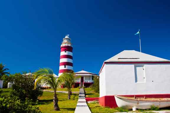 Red and white candy cane striped lighthouse on Elbow Cay, Abaco, Bahamas, Hope Town. Storage shed with small boat are in the foreground. Copy space available in the clear blue sky
