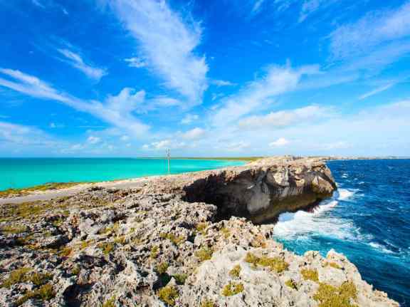 The Eleuthera land bridge, also known as the Glass Window Bridge, is a natural limestone arch that spans across Queen's Highway, connecting the northern and southern parts of Eleuthera Island in the Bahamas. The bridge provides a striking visual contrast between the dark blue waters of the Atlantic Ocean on one side and the calm turquoise waters of the Exuma Sound on the other.