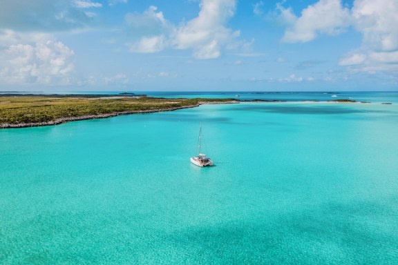 This image depicts a lone yacht floating in the shallow, tranquil waters surrounded by the natural beauty of the cay’s landscape. The vibrant turquoise of the water contrasts strikingly with the lush greenery of the cay, creating a serene and inviting atmosphere for any sailor or visitor.