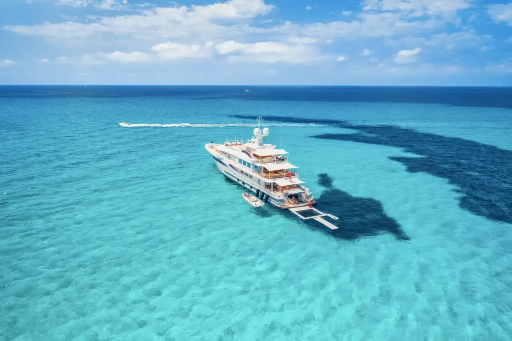 A motor yacht at anchor in clear turquoise Bahamian water, with a tender and swimming platform